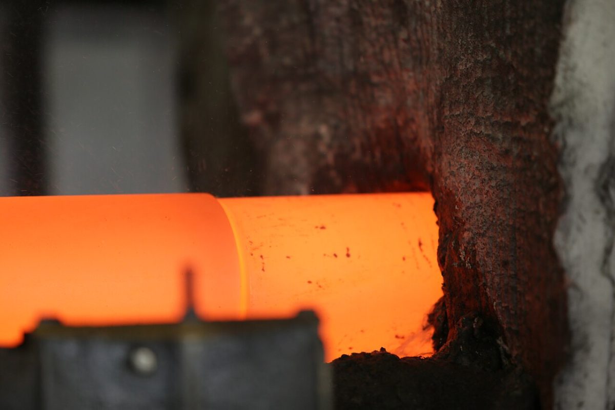 Induction-heated steel billet glowing orange, prepared for piercing and ring rolling