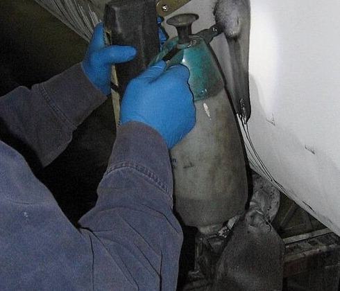 Technician's gloved hands performing wet magnetic-particle inspection on a steel pipe surface